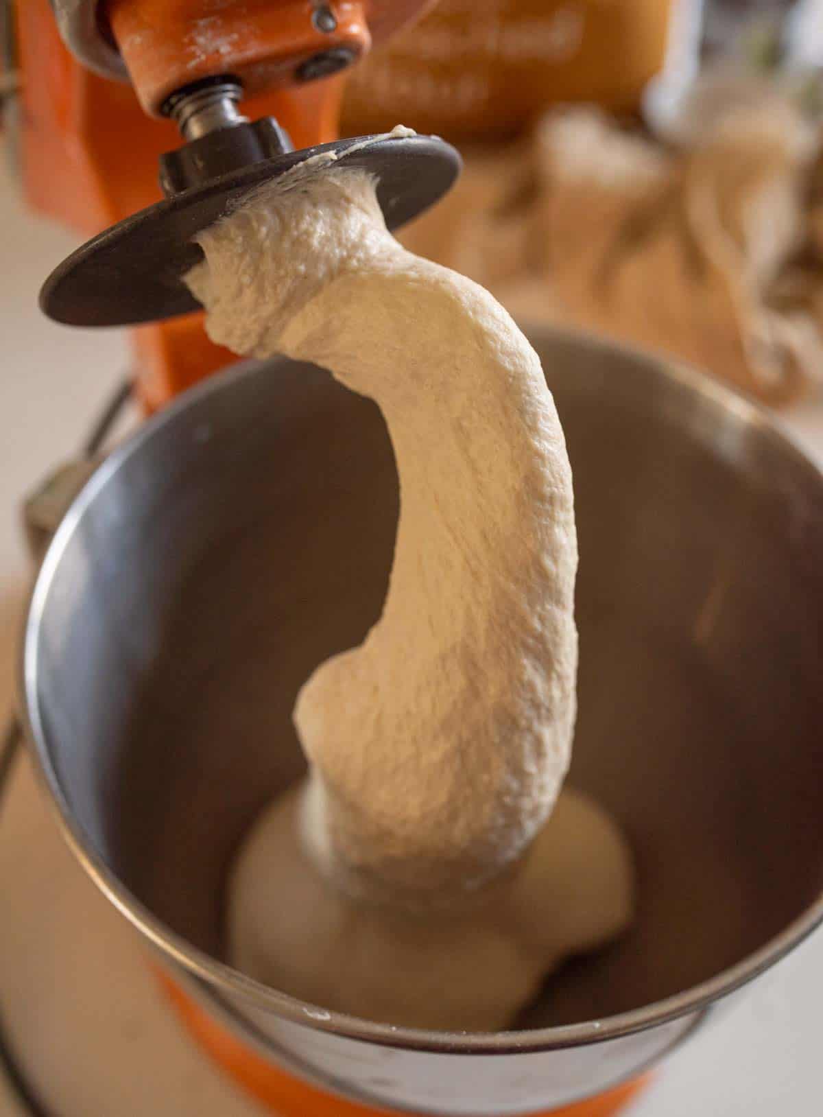 baquette dough in stand mixer bowl with dough hook covered in dough.