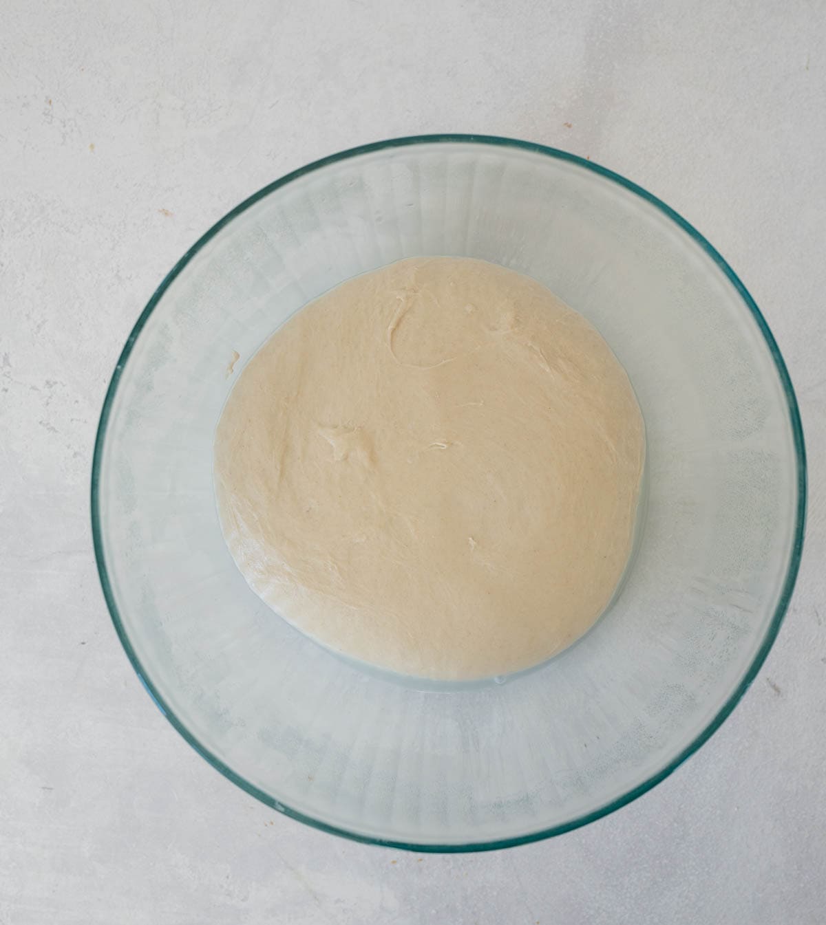 rising ball of bread dough in clear class bowl.