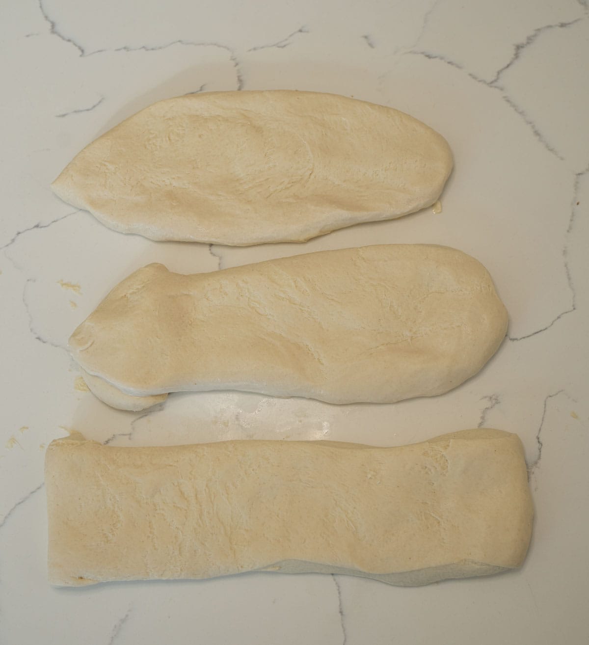 baguette dough split into three pieces on white countertop.