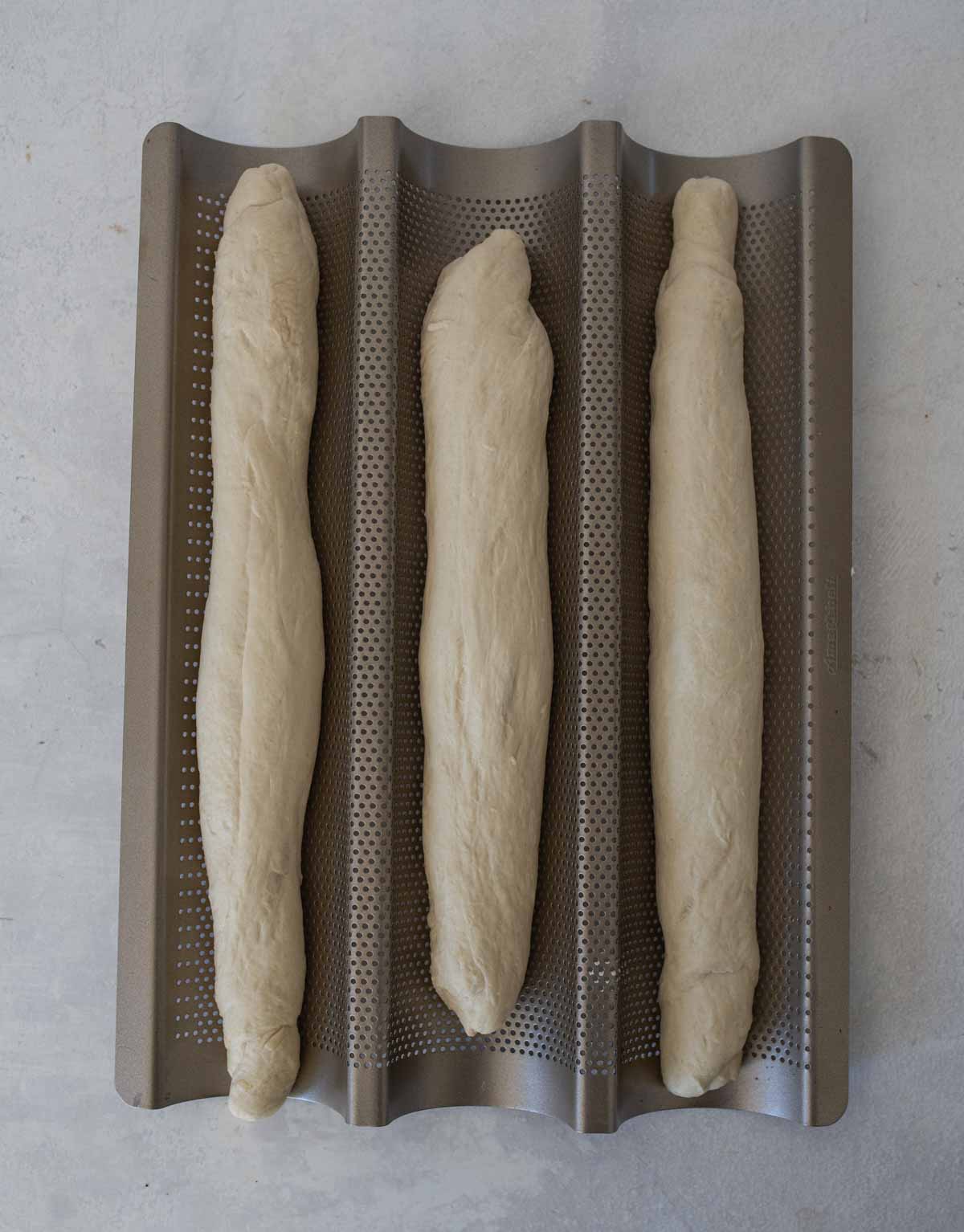 three pieces of dough in metal baguette pan.