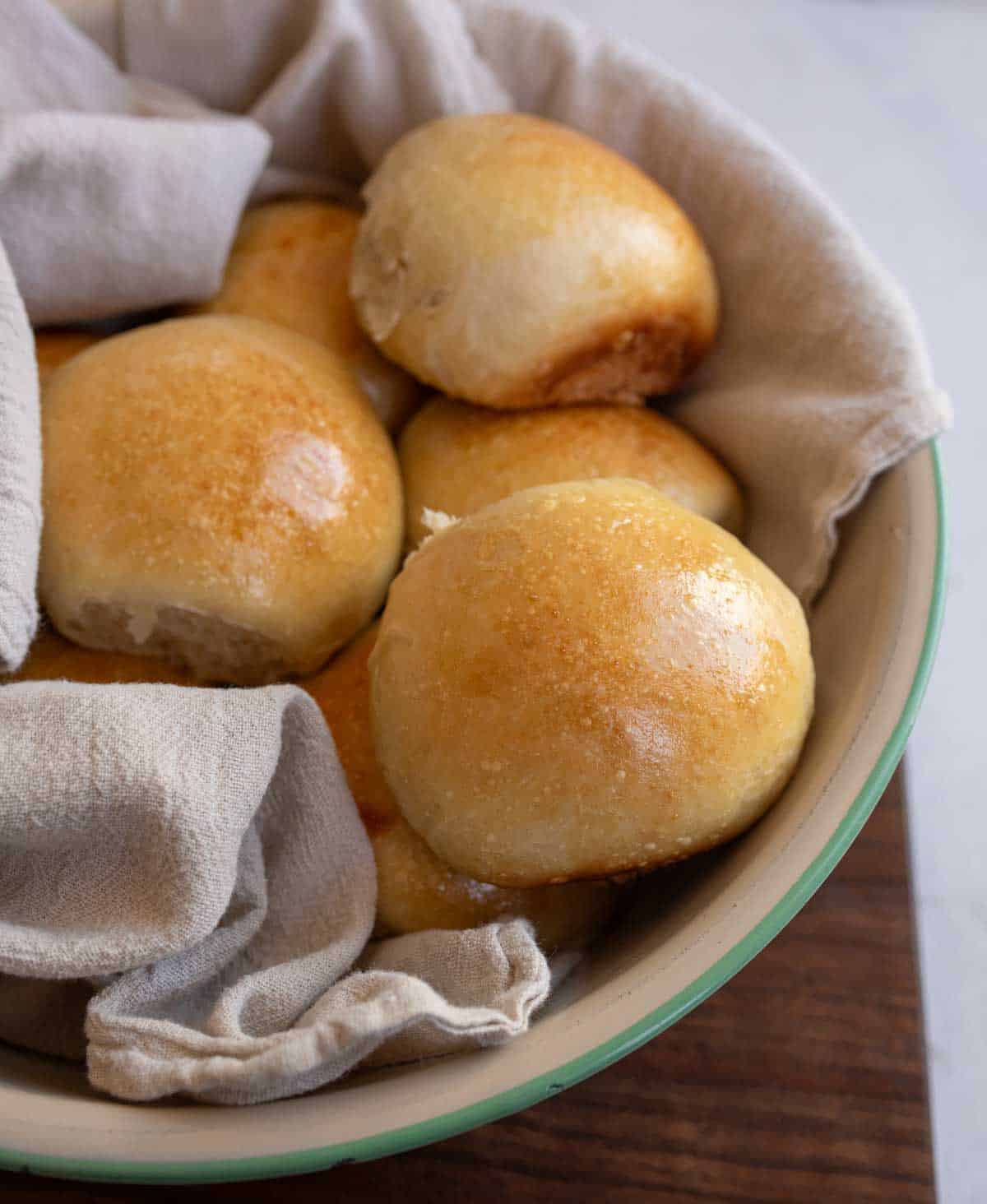 golden brown rolls in white and blue bowl with a towel.