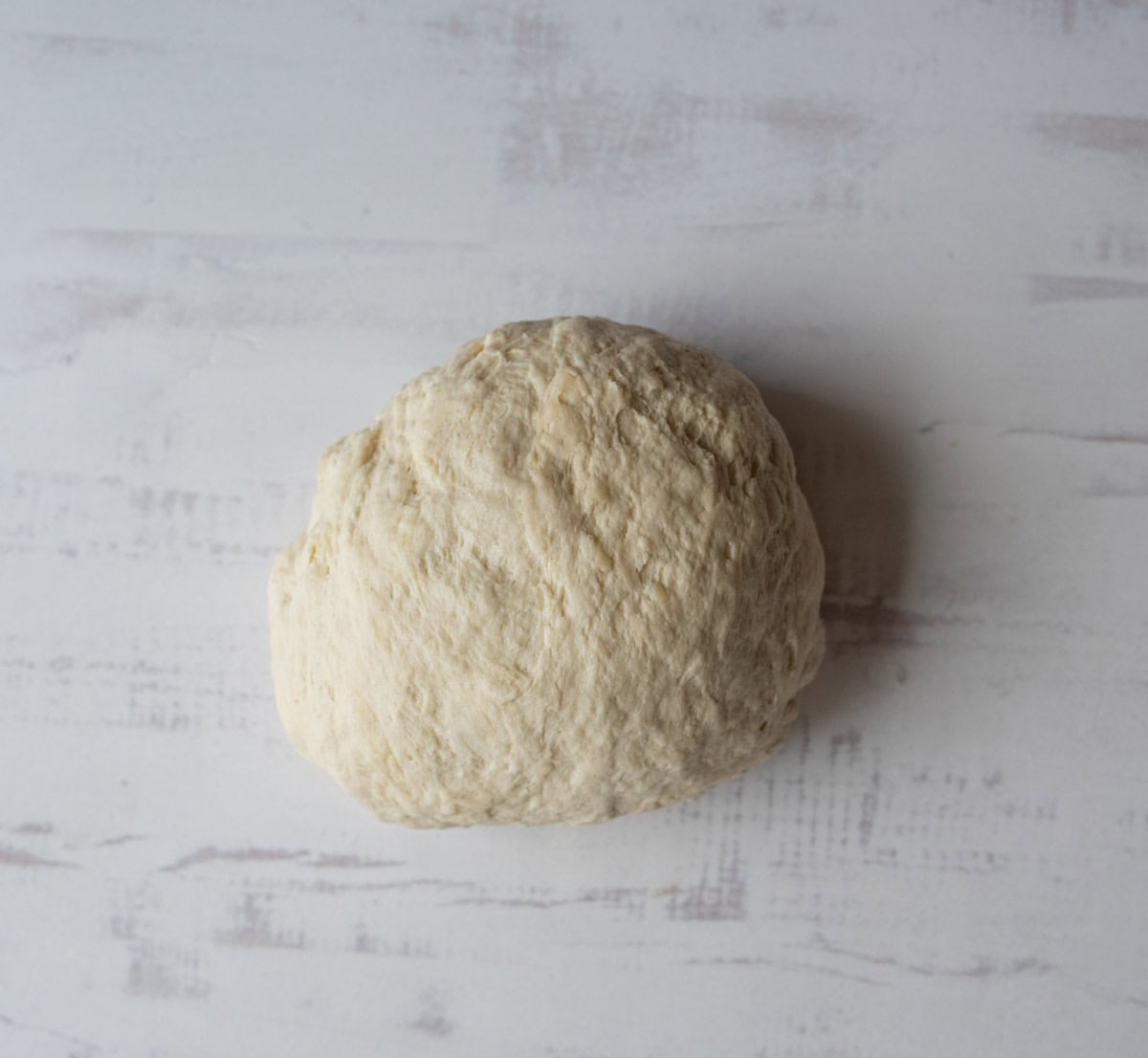 ball of sourdough tortilla dough on white countertop.