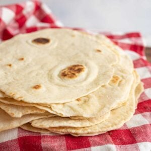 pile of cooked tortillas on red and white checked towel.