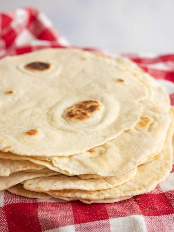 pile of cooked tortillas on red and white checked towel.