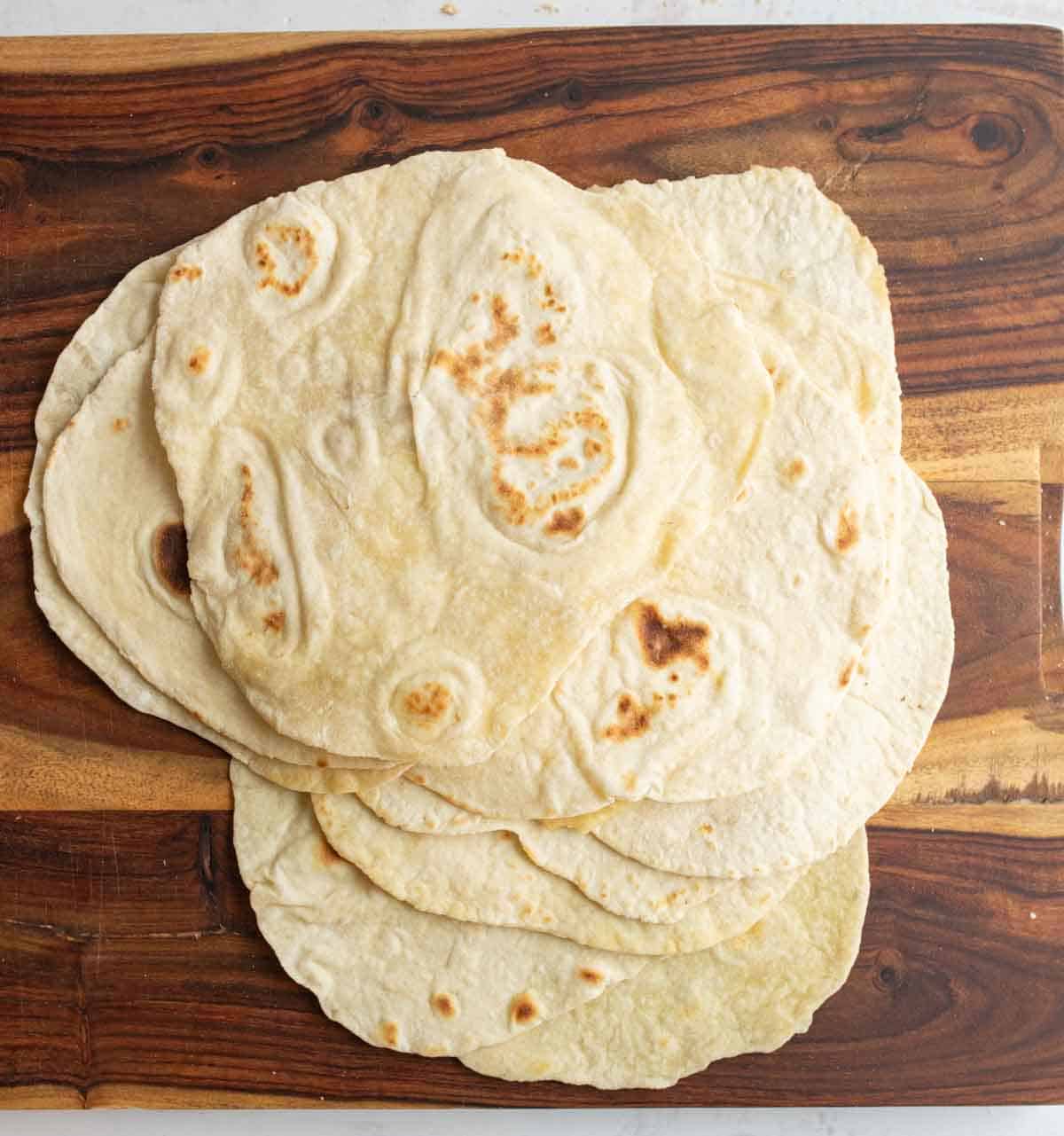 pile of cooked tortillas on brown board.