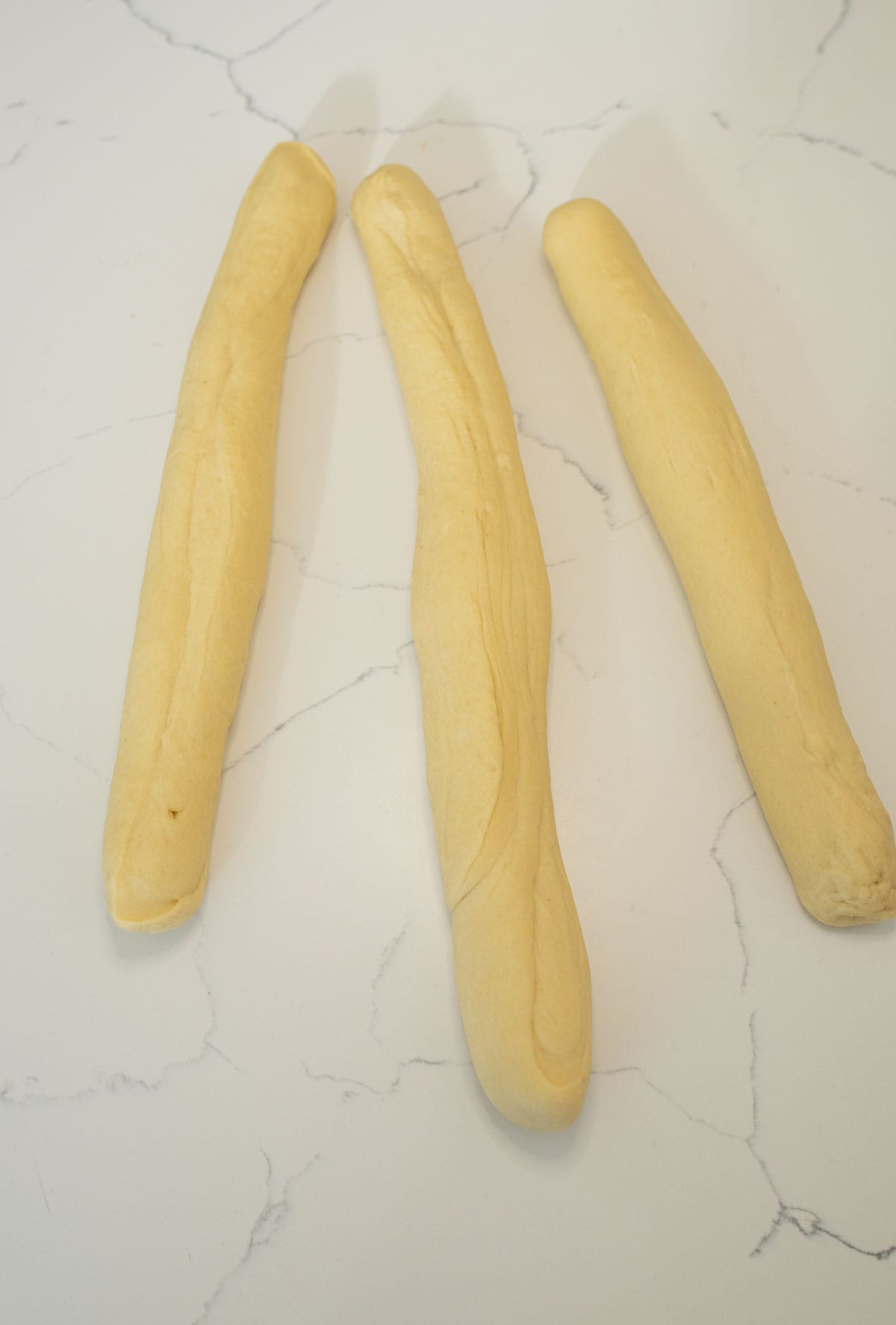 three long ropes of sourdough challah bread dough on white counterop.