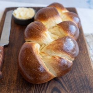 baked sourdough challah bread on brown board with knife and bowl of butter.