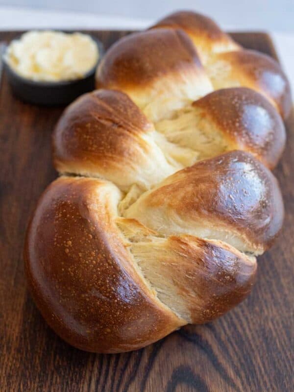 baked sourdough challah bread on brown board with knife and bowl of butter.