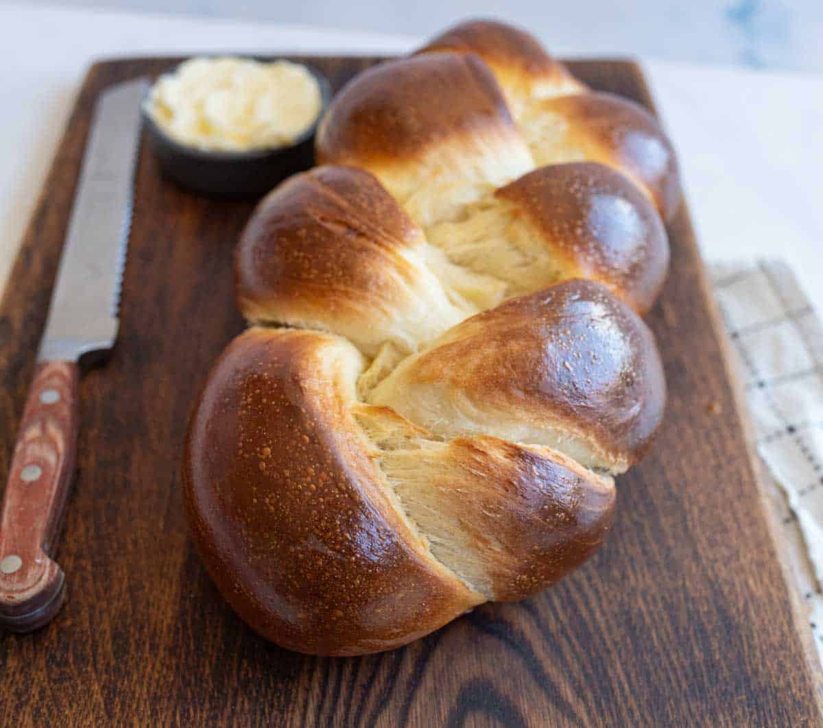 baked sourdough challah bread on brown board with knife and bowl of butter.