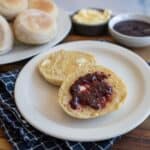 split baked english muffin on white plate with butter and jelly.