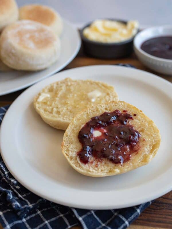 split baked english muffin on white plate with butter and jelly.