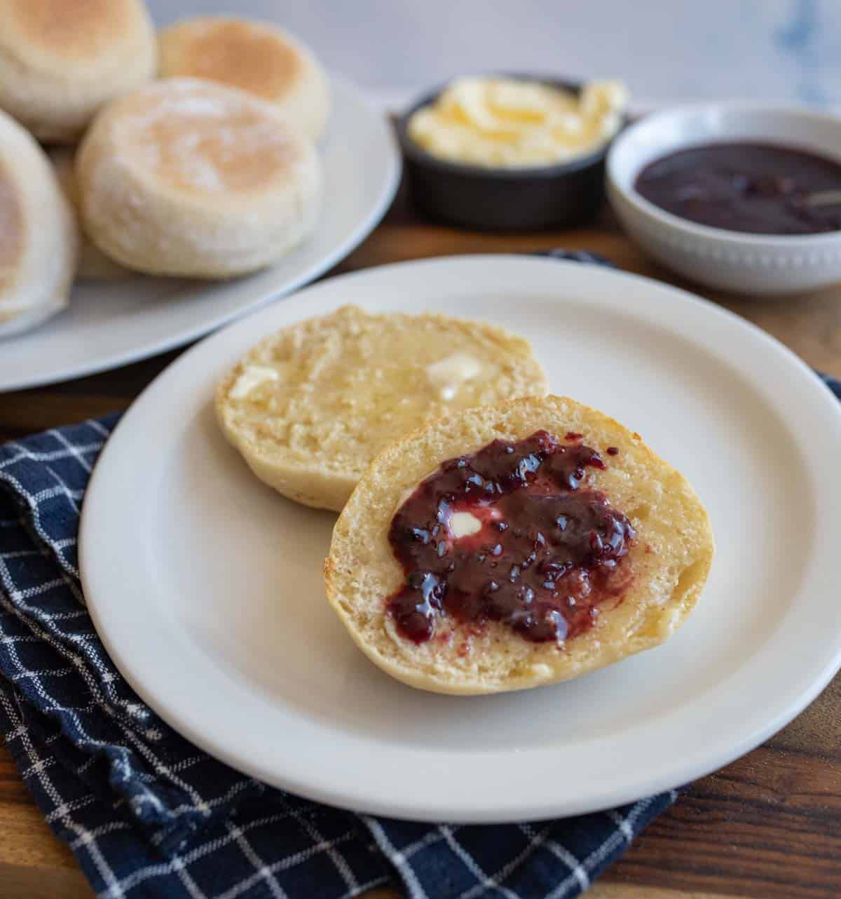 split baked english muffin on white plate with butter and jelly.