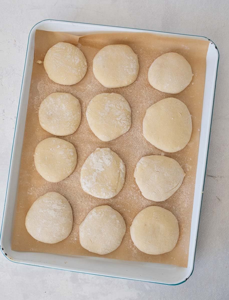 unbaked sourdough english muffins on white sheet pan.