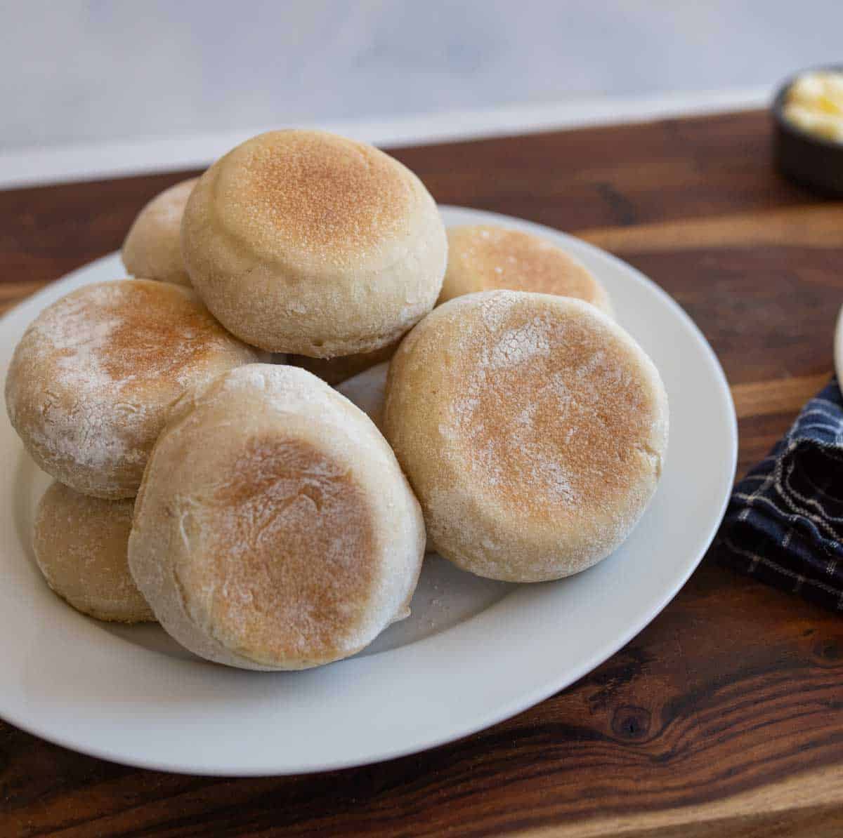 pile of baked sourdough english muffins on white plate.