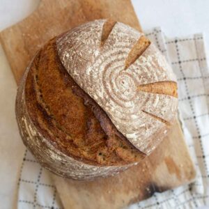 round loaf of sourdough rye bread on brown wooden board.