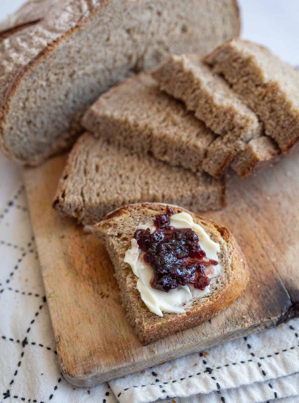 slices of bread on wooden board with butter and jam on one slice.