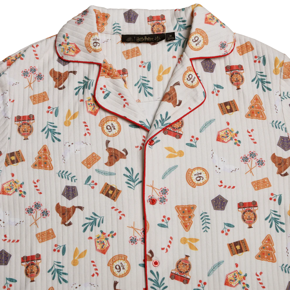 A festive pajama shirt with a Harry Potter theme, featuring symbols like the 9¾ train platform, magical creatures, candy, and Christmas trees. The shirt is white with red piping and colorful illustrations scattered throughout.