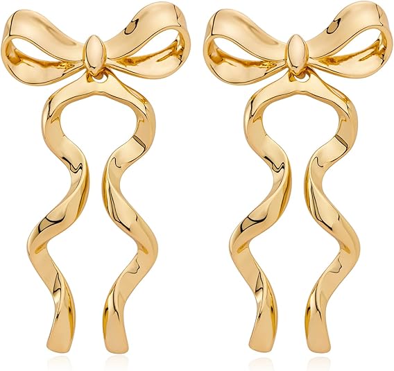 A pair of shiny gold earrings shaped like elegant bows with wavy ribbons hanging down, set against a white background.