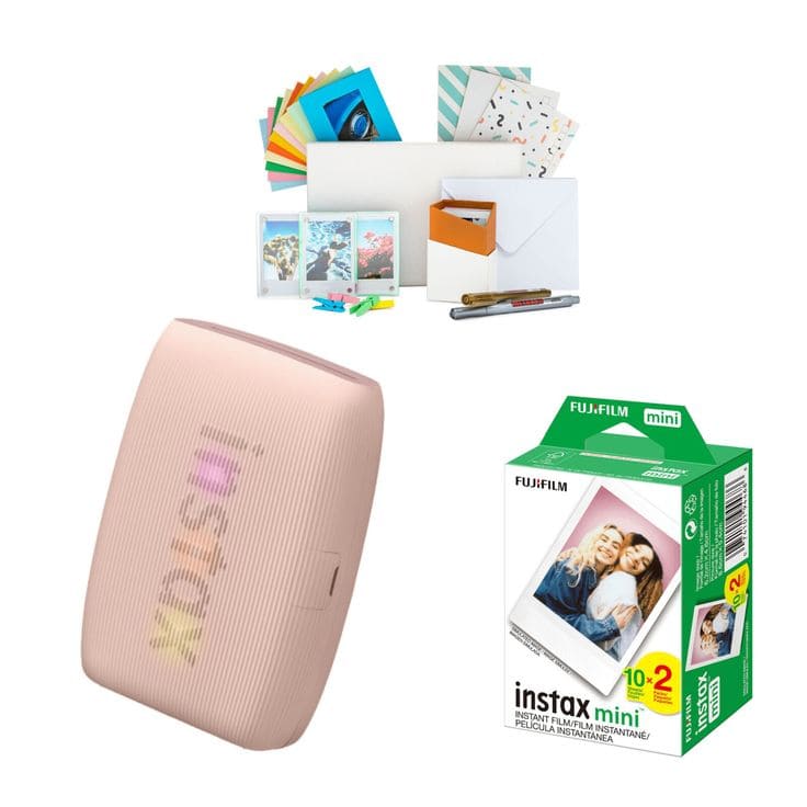 A pastel pink Fujifilm Instax printer, a box of Instax mini film, and an assortment of colorful paper, envelopes, and markers are arranged on a white background.