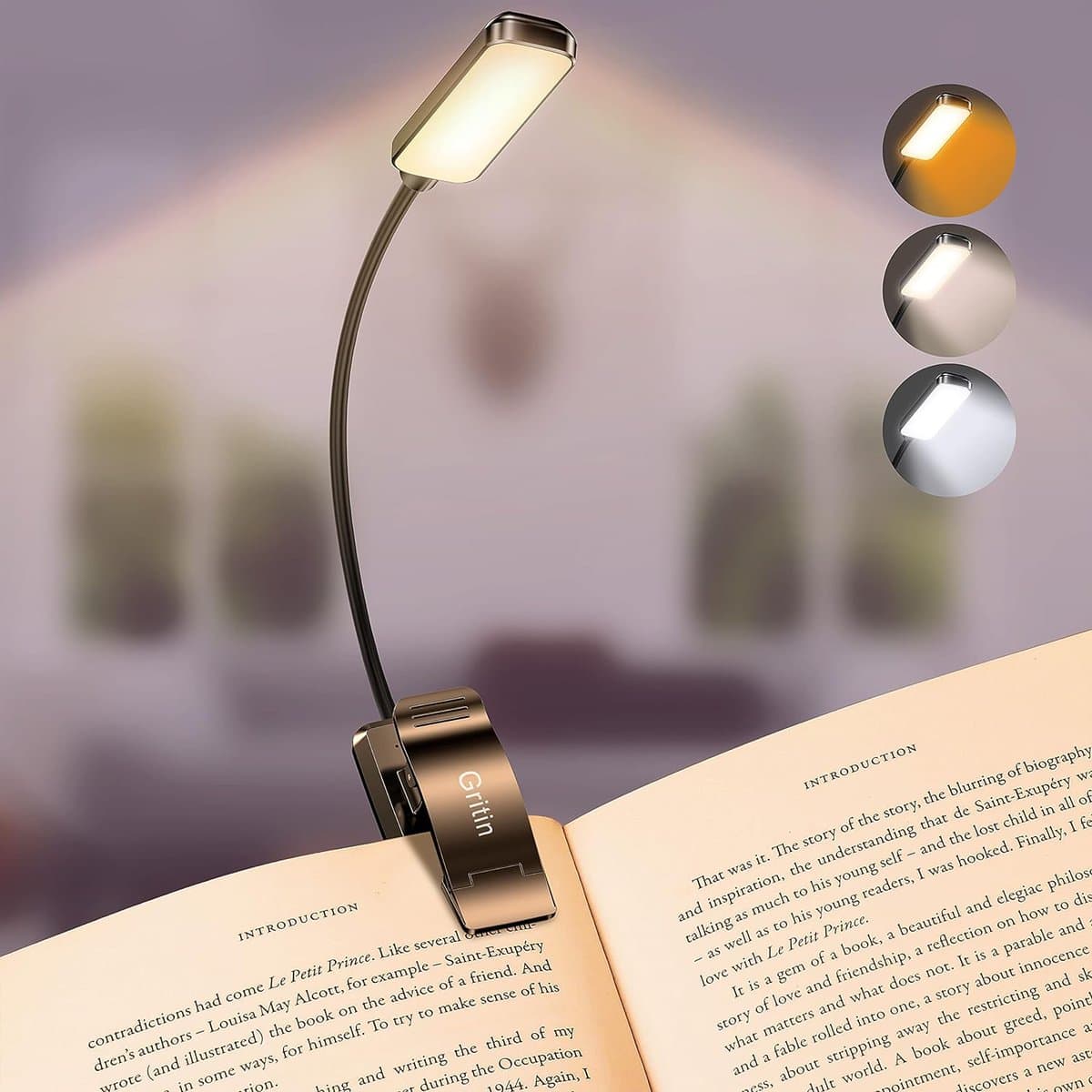 A book light clipped onto an open book, illuminating the pages. The light has a flexible neck and offers three lighting modes: warm, cool, and mixed, shown in circular icons. The background is a softly blurred room.