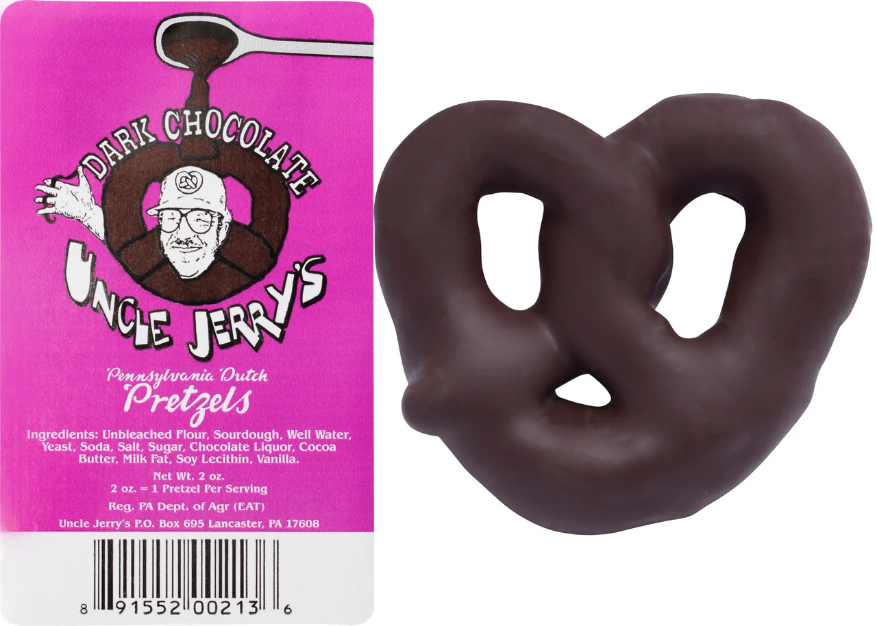 A dark chocolate-covered pretzel rests beside pink packaging labeled Uncle Jerry's Pennsylvania Dutch Pretzels, featuring a cartoon man. With ingredients like flour, sourdough, well water, and cocoa butter, it's perfect for gift-giving ideas for Christmas.