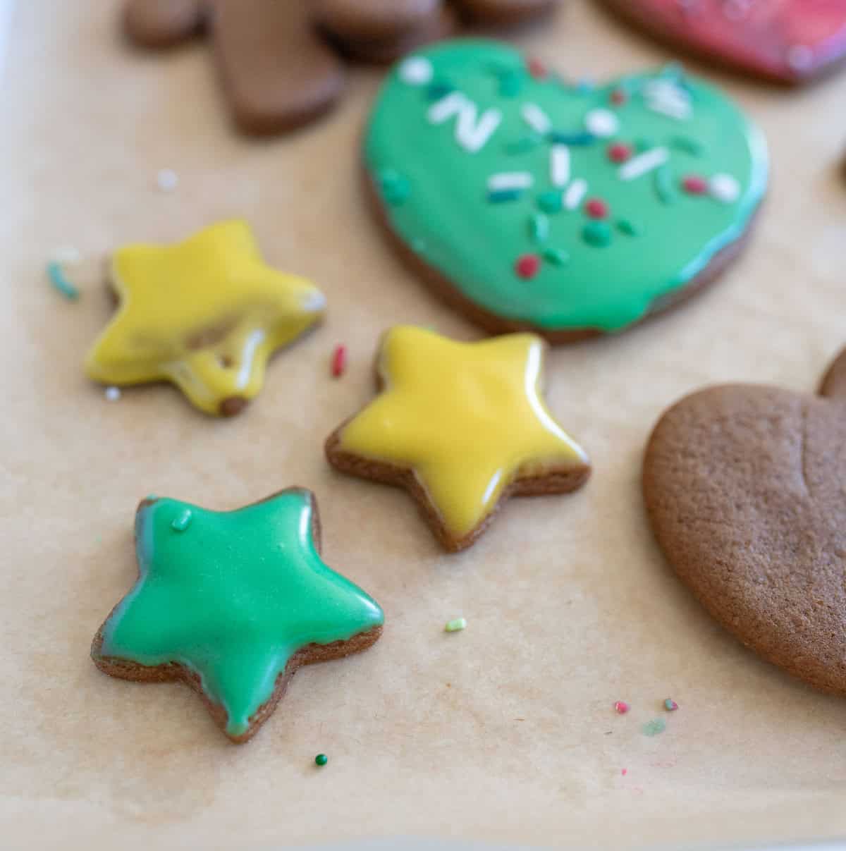 A tray featuring star-shaped cookies, iced in green and yellow, and a heart-shaped cookie decorated with green icing and sprinkles. The cookies are on parchment paper.