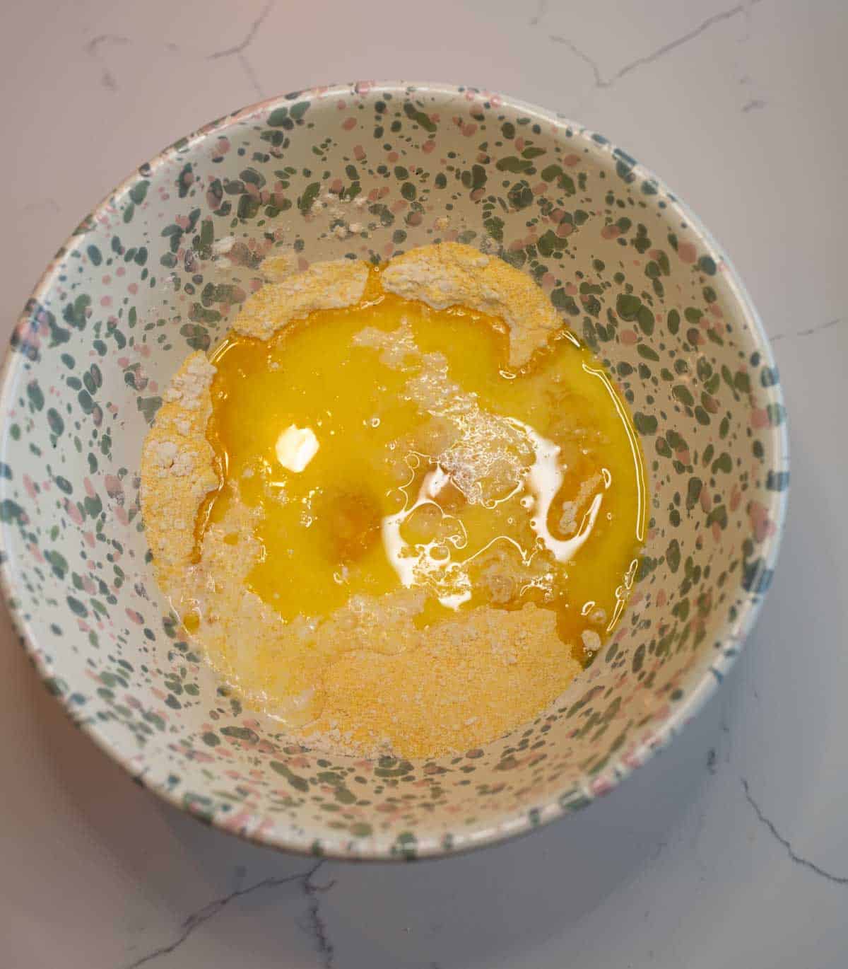 A speckled bowl contains a raw egg, partially mixed with flour. The ingredients are ready for blending, resting on a light-colored countertop.