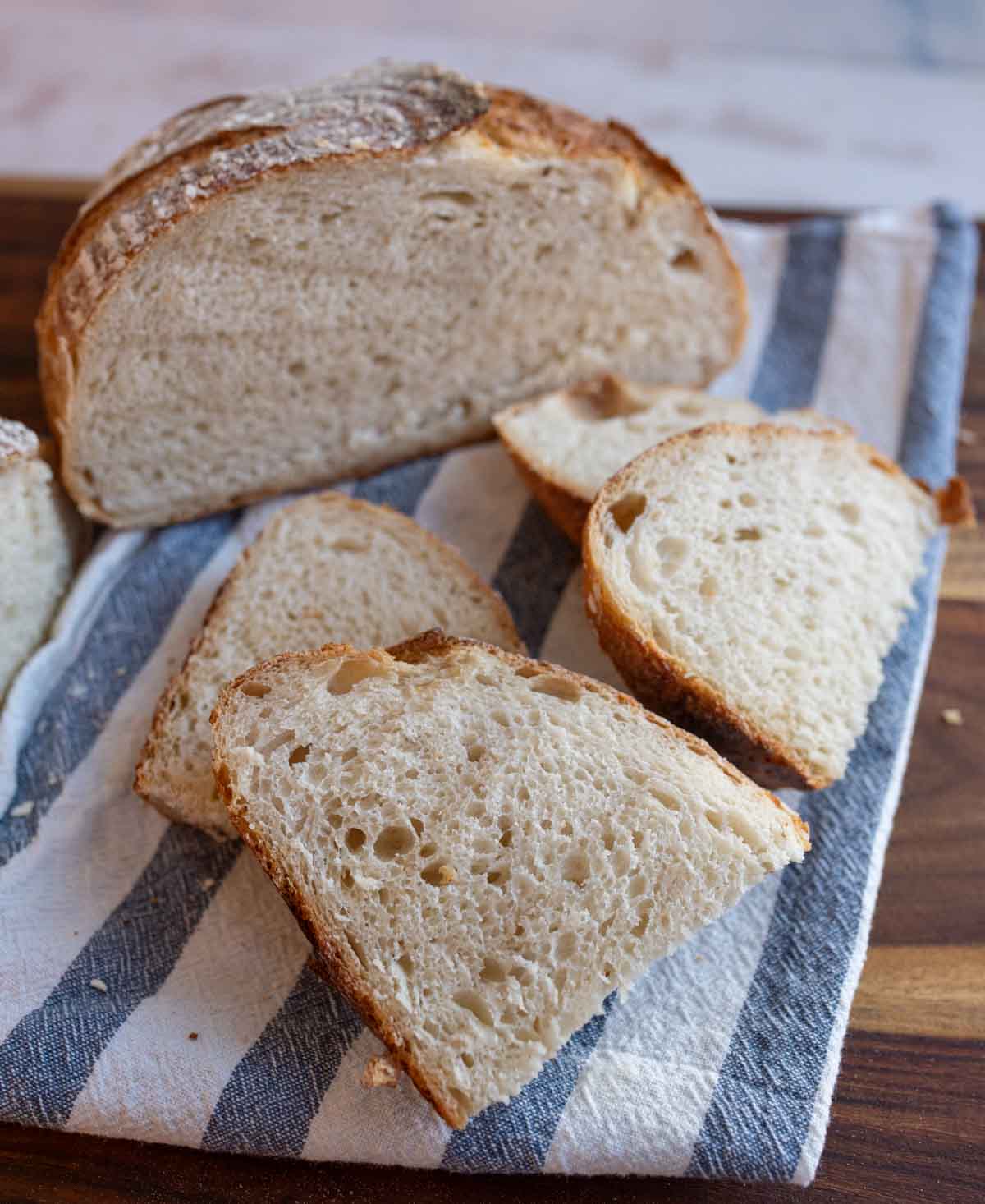 round loaf of no knead sourdough bread cut into a half and slices on blue and white towel.