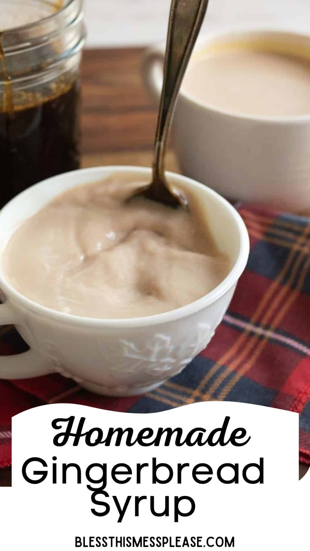 A cup of warm frothy drink with a spoon inside, next to a cup of gingerbread syrup on a plaid cloth. Text reads Homemade Gingerbread Syrup with a website link below.