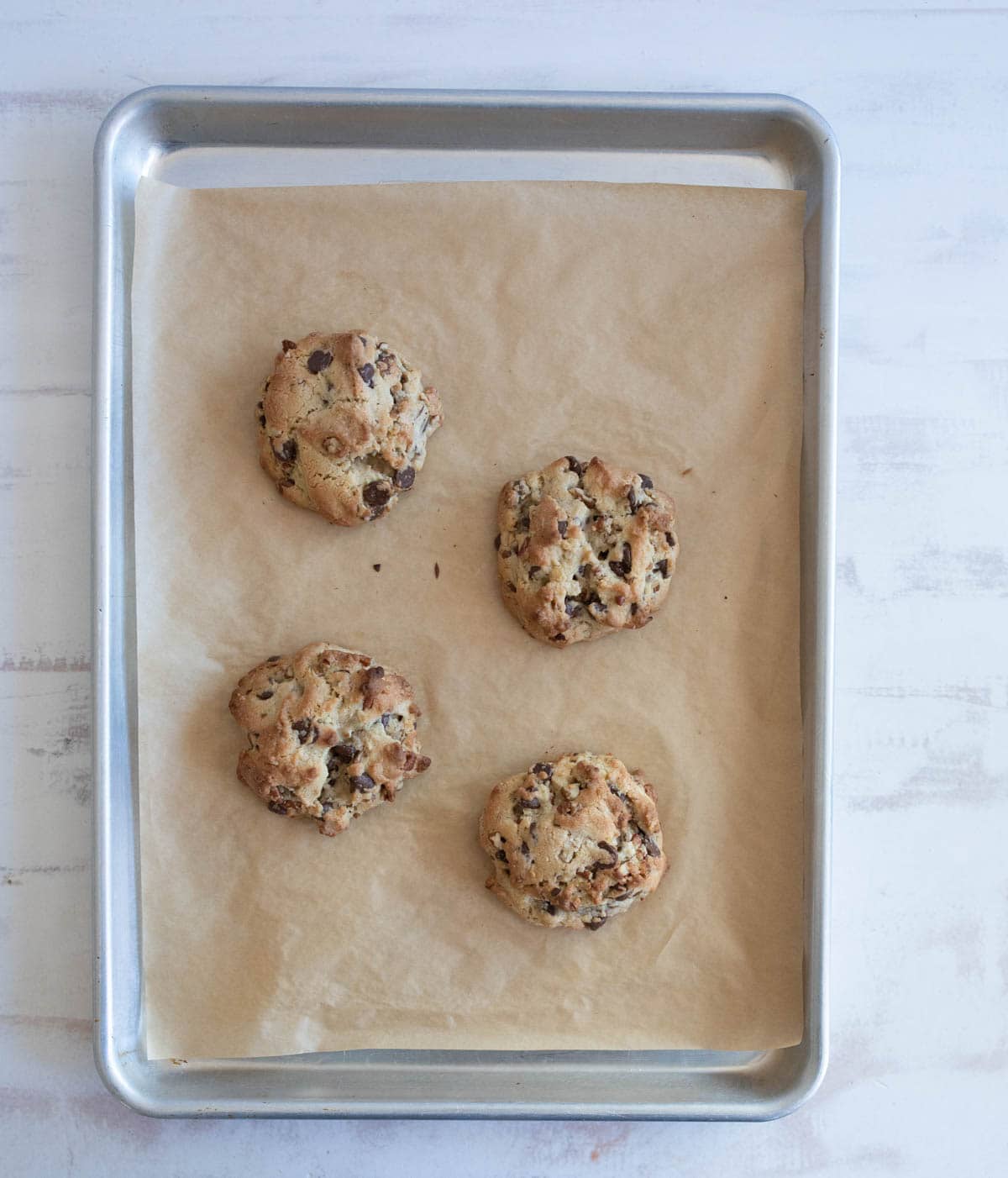 Four freshly baked chocolate chip cookies on a parchment-lined baking sheet.