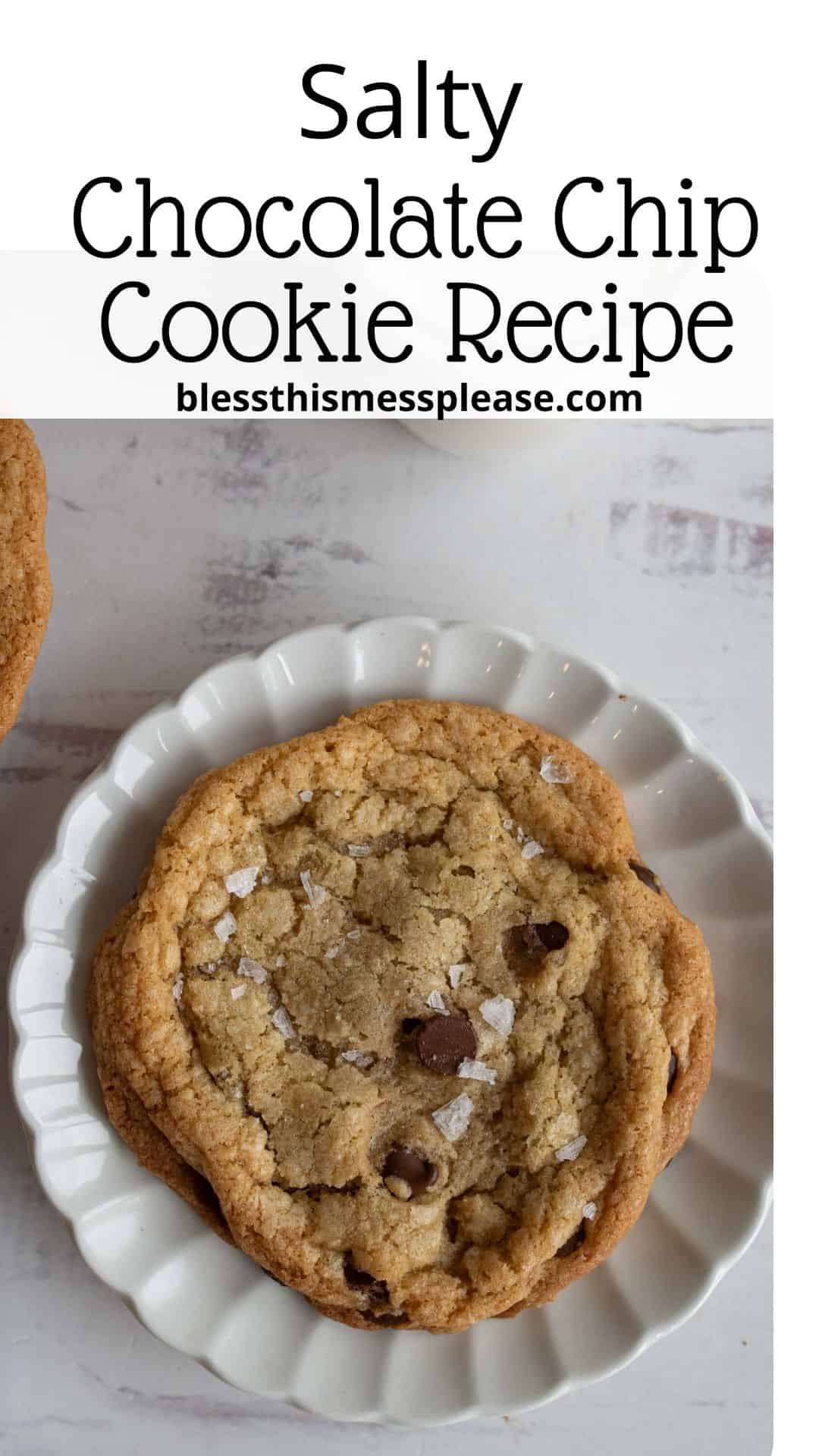 A chocolate chip cookie sprinkled with sea salt sits on a fluted white plate. The background shows a light-colored surface, and above the cookie, text reads Salty Chocolate Chip Cookie Recipe with a website URL.