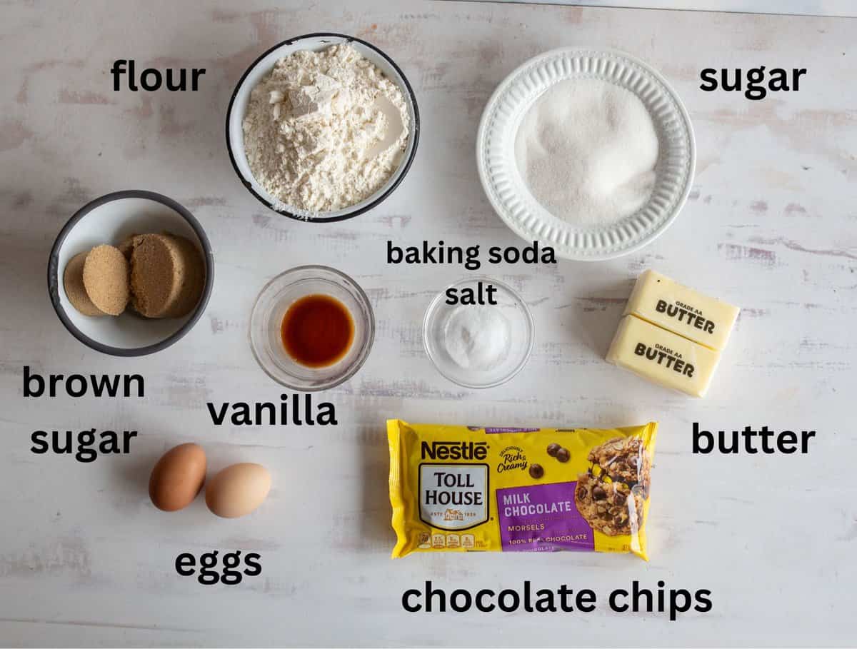 Baking essentials are neatly arranged on the table: flour, sugar, brown sugar, butter, eggs, vanilla extract, baking soda, salt, and a package of Nestlé Toll House milk chocolate chips—everything needed to create scrumptious Nestlé Toll House cookie bars.