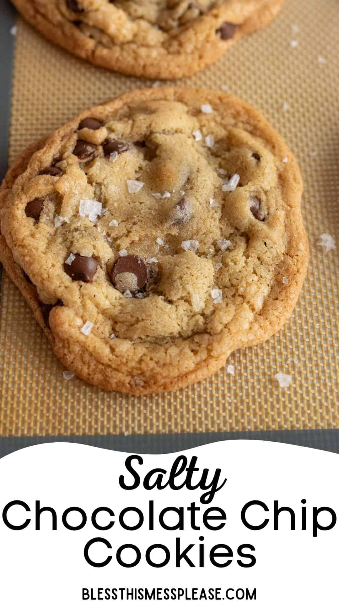 Close-up of a freshly baked chocolate chip cookie topped with sea salt flakes on a baking mat. The text Salty Chocolate Chip Cookies is displayed below.